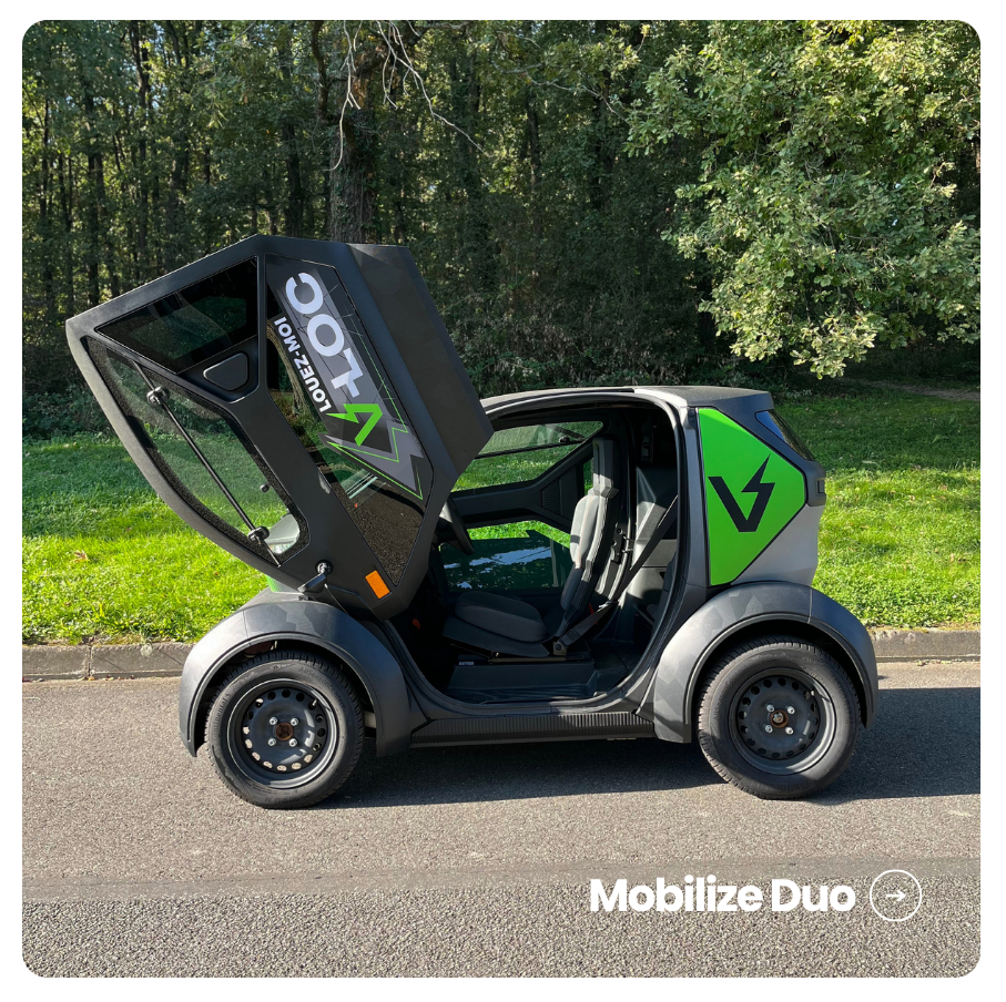 Mobilize Duo noir et vert de profil avec la porte en élytre ouverte, sur une route bordée d'arbres.