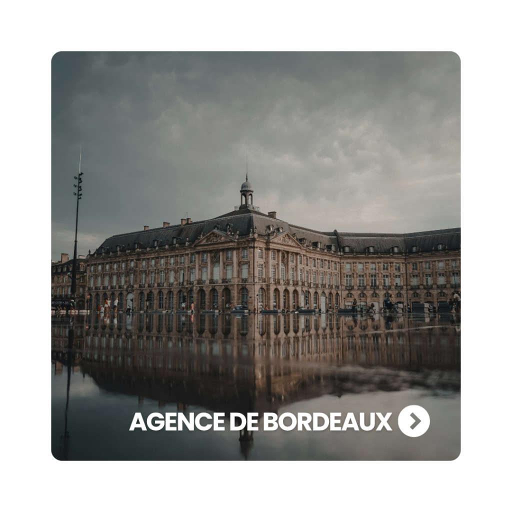 La place de la Bourse à Bordeaux et le Palais de la Bourse se reflétant sur la surface d'eau du Miroir d'eau par temps couvert.